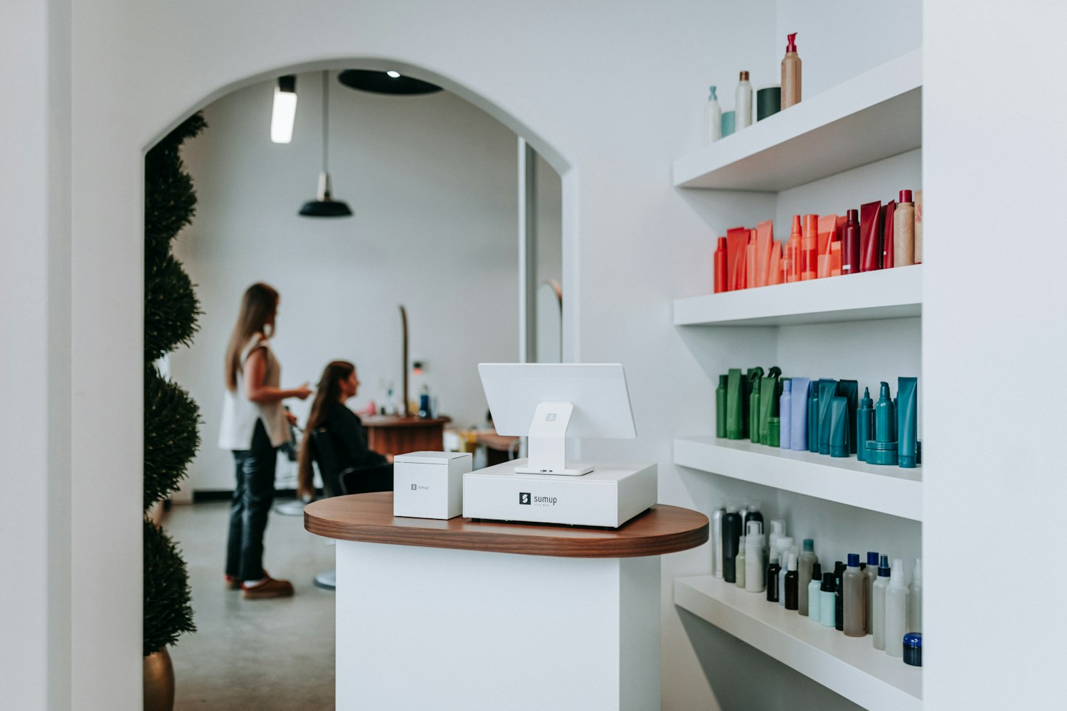 A bright salon reception desk with product shelves and an arched doorway